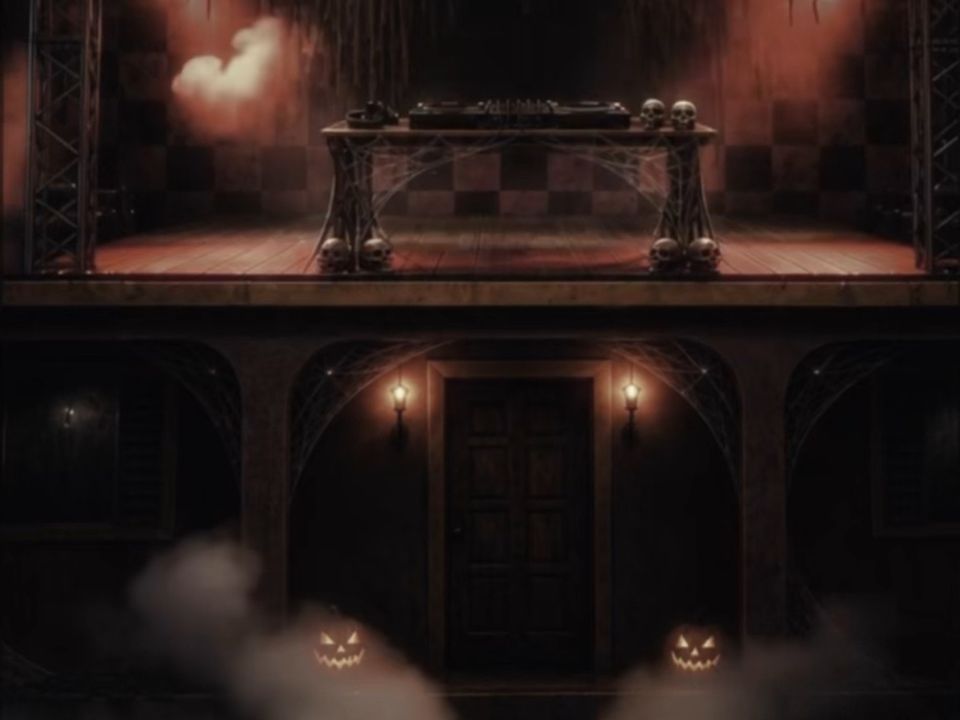 A dark room inside the house: a chandelier hanging in smoke over a long table, lanterns at either side, jack-o&rsquo;-lanterns on the steps and arched doorways below.